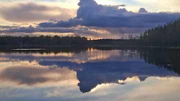 Rauhallinen järvimaisema auringonlaskun aikaan, jossa pilvet heijastuvat tyynen veden pintaan.