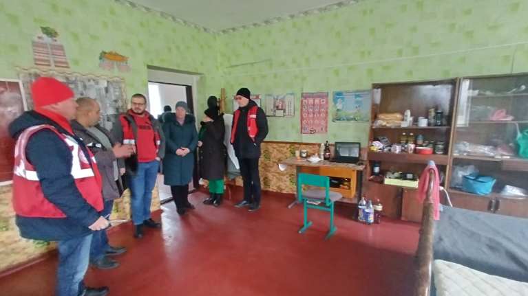 Ryhmä talvitamineisiin ja Punaisen Ristin punaisiin huomioliiveihin pukeutuneita ihmisiä huoneessa, jossa on vihertävät tapetit. 