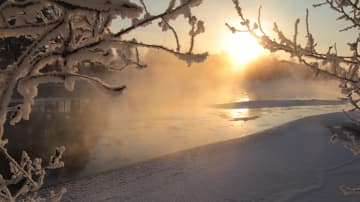 Kylmä päivä Siikalatvalla. Joki savuaa ja aurinko paistaa sumun takaa. 