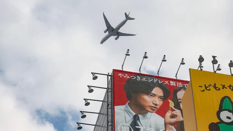 Matkustajalentokone lentää pilvenpiirtäjien yllä Tokiossa.