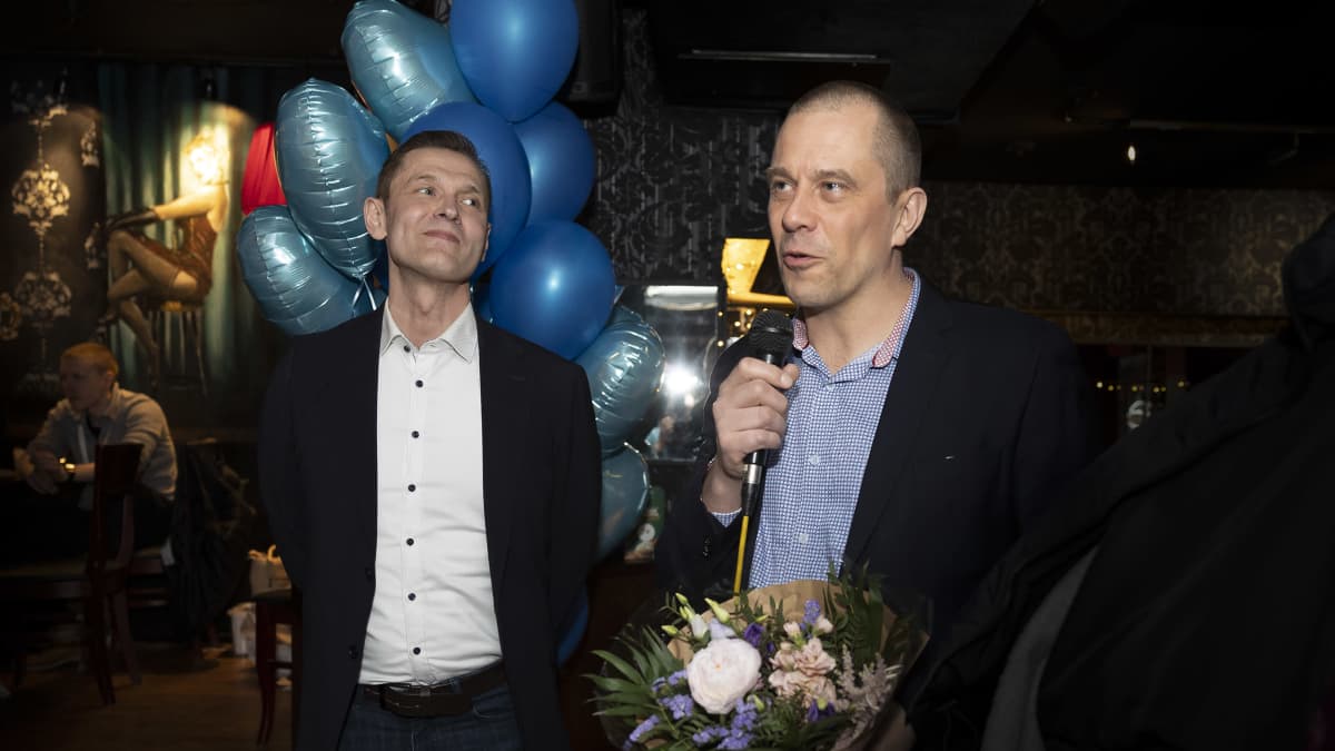 Sinuhe Wallinheimo kuuntelee hymyillen, kun Ville Väyrynen puhuu kukkakimppu kädessään Kokoomuksen vaalivalvojaisissa.