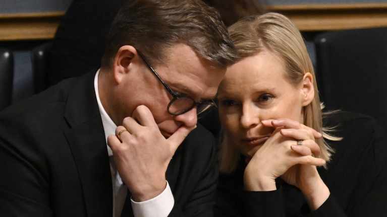 Pääministeri Petteri Orpo ja valtiovarainministeri Riikka Purra kuiskuttelevat toisilleen eduskunnassa ministeriaitiossa.