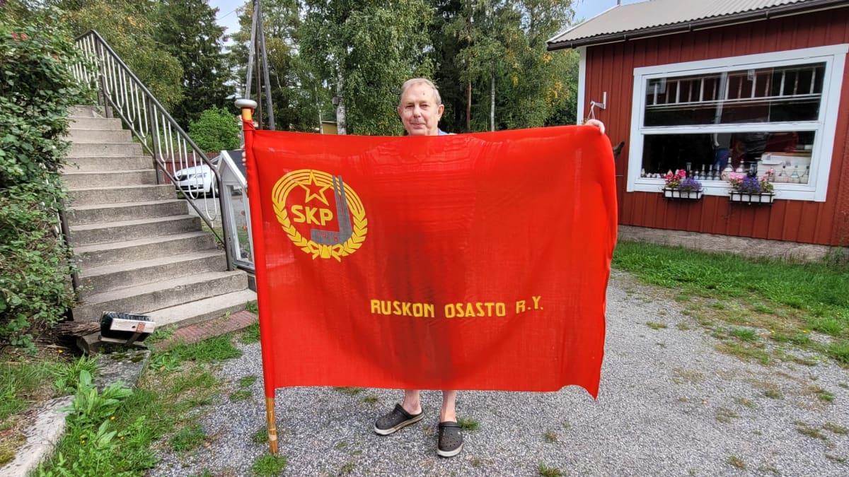 Mies pitää suurta, punaista lippua, jossa on Suomen kommunistisen puolueen logo ja teksti "Ruskon osasto ry".