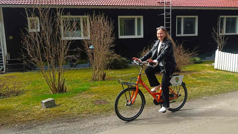 Sastamalan matkailun kesäharjoittelija Peea Pajunen ajaa kaupunkipyörällä hiekkatietä talon edustalla.