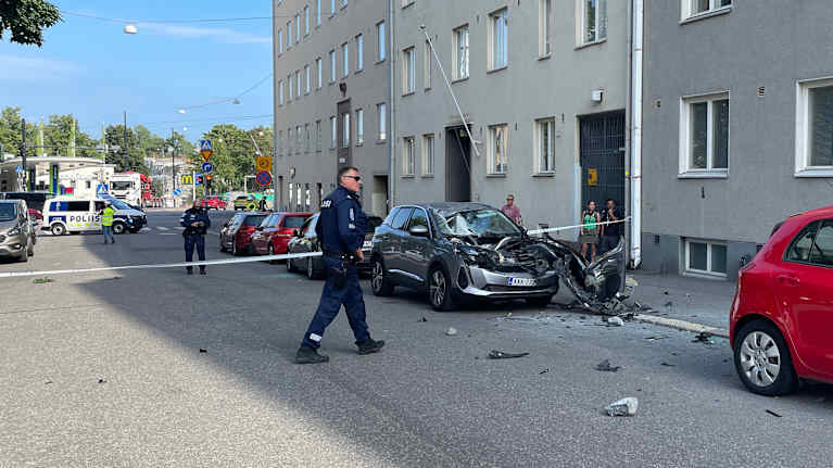 Police on the street, a half-destroyed car and onlookers on the street.