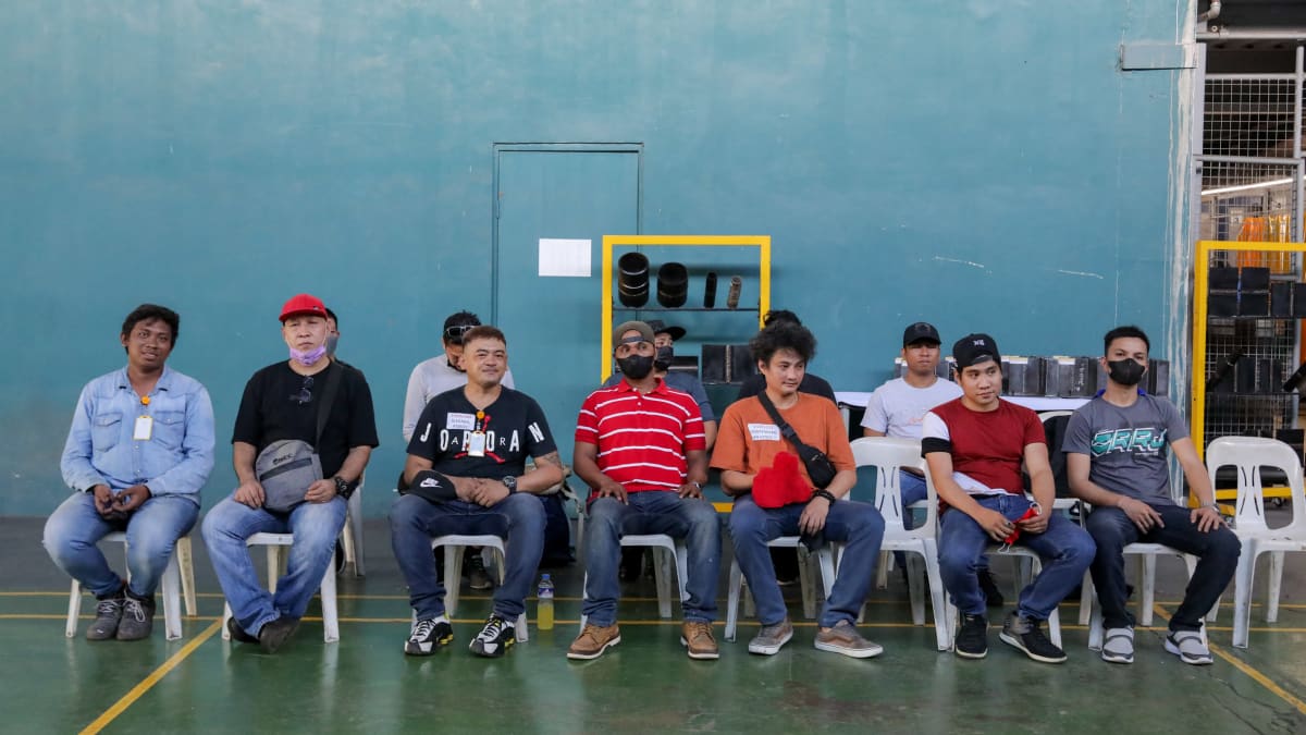 Filippiiniläisiä, eri näköisiä miehiä istuu kahdessa rivissä odottamassa vuoroaan. 