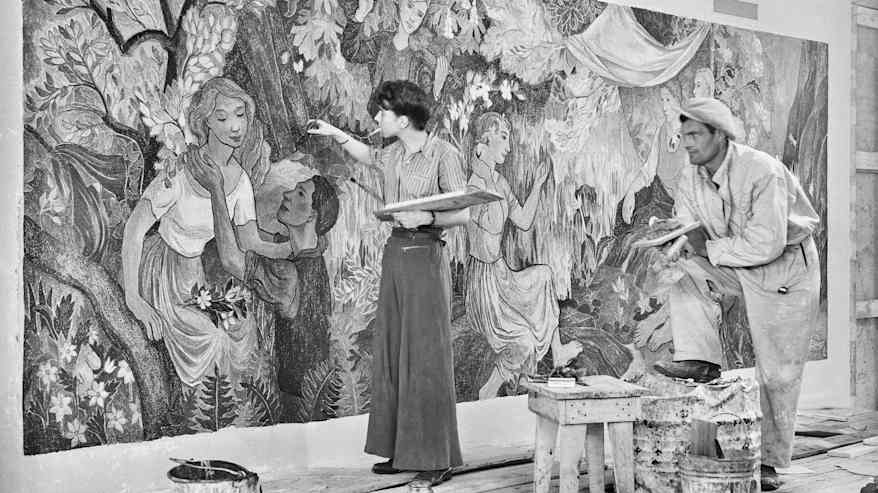 Mustavalkoisessa valokuvassa housuasuinen nainen maalaa seinäfreskoa savuke suussa, vieressä katsoo työvaatteissa mies polveensa nojaten.