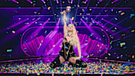 Erika Vikman on her knees in a rain of confetti. Vikman raises the UMK trophy in the air with one hand.