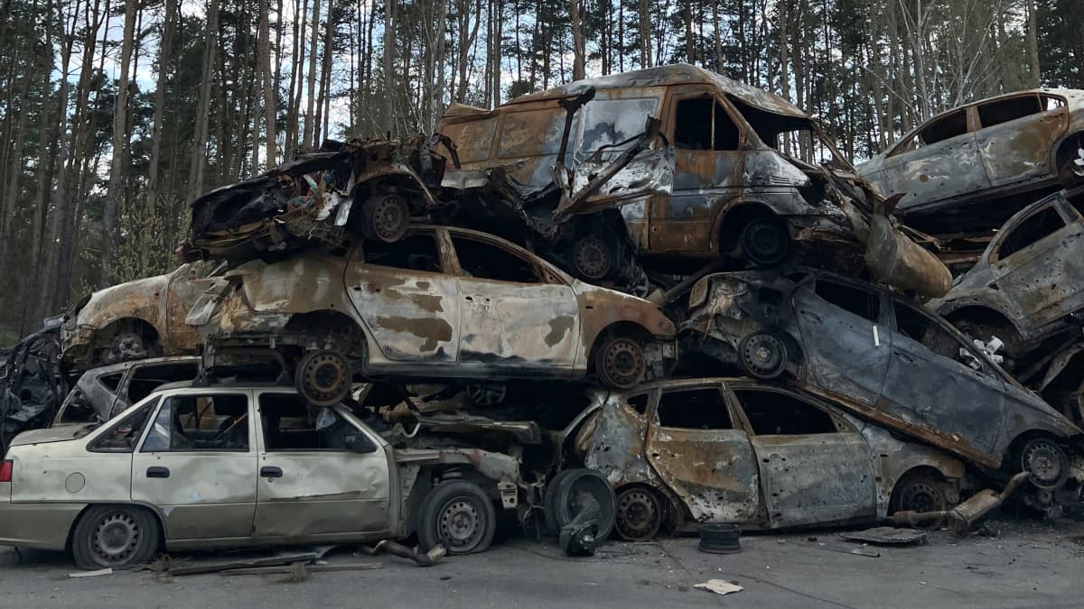 Päällekkäin kasattuja tuhoutuneita autoja metsänrajassa.