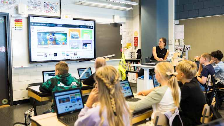 Opettaja Helmiina Luoma näyttää isolta ruudulta Adobe Express-pääsivua pulpettien takana istuville nuorille oppilaille.
