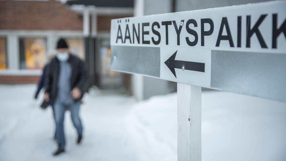 Kyltti äänestyspaikalle ja kaksi ihmistä kävelee ulos rakennuksesta.