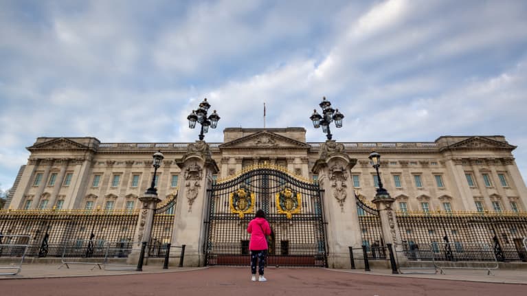 Nainen seisoo selkä kameraan päin Buckinghamina palatsin edessä.