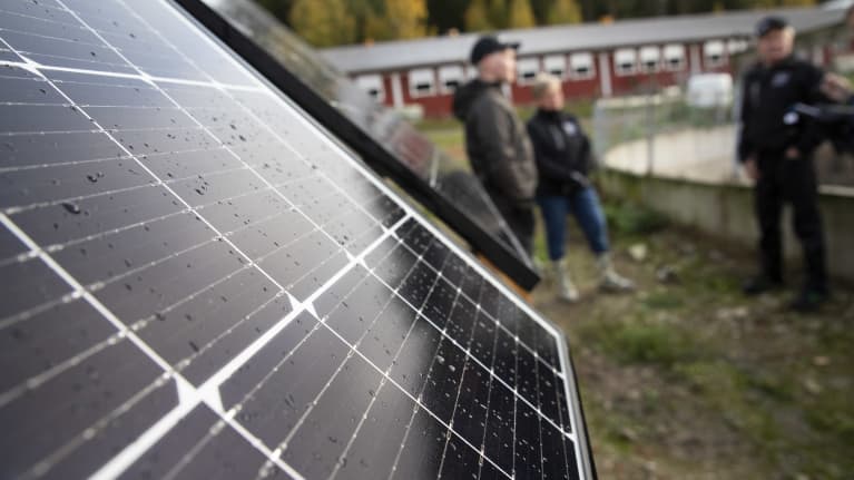 Maatilan aurinkopaneeleja. Taustalla seisovat maatalousyrittäjät Juha-Matti, Anneli ja Jouni Laukkanen