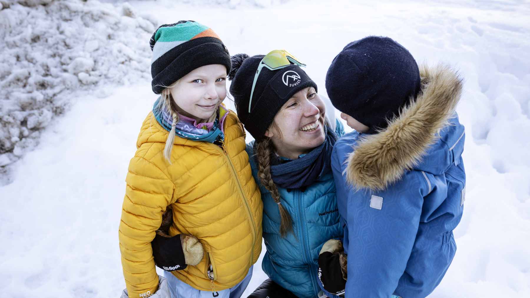 Susanna Ylinen halaa lapsiaan ja hymyilee. Toinen lapsista katsoo suoraan kameraan.