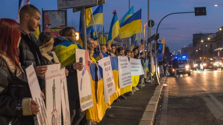Ukrainan lippuja pitelevät ihmiset seisovat kadulla.