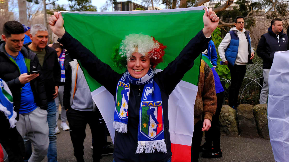 Viher-valko-punaiseen peruukkiin sonnustautunut nainen pitelee Italian lippua päänsä yläpuolella