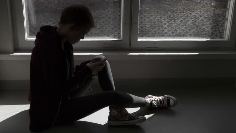 A child using a smartphone, sitting by a window in the dark. 