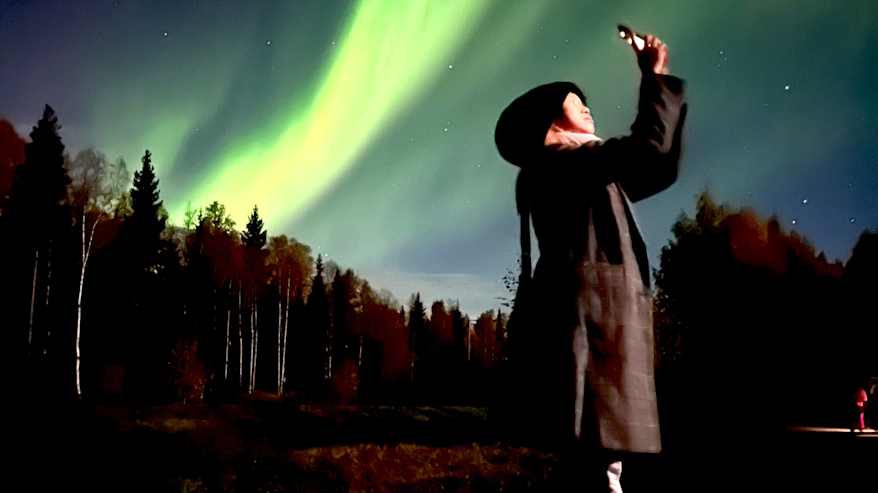 Nainen kuvaa revontulia älypuhelimella. 