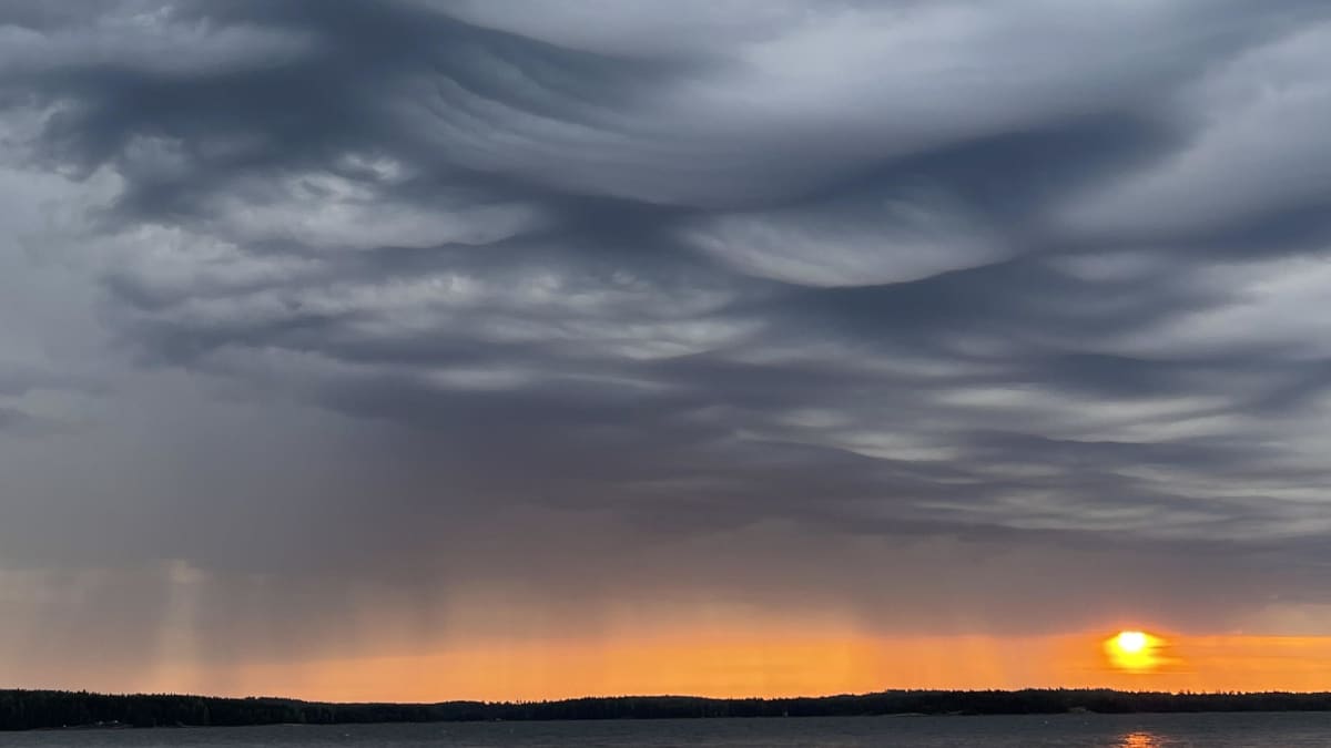 Aamun taivas Virolahdella. Merimaisemaa, aurinko horistontissa ja uhkaavia pilviä taivaalla. 