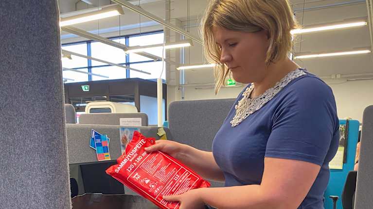 Asumisneuvoja pakkaa sammutuspeitteen isoon kestokassiin, jossa on kodintavaroita. 