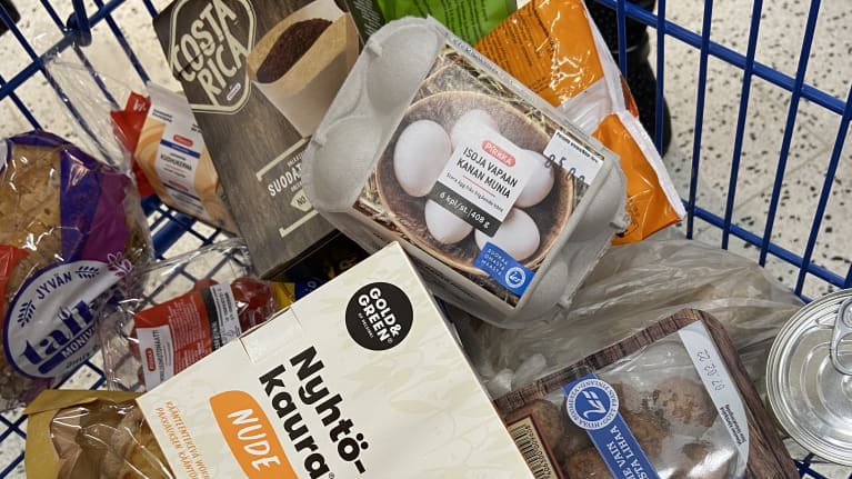 Ostoskärryt, missä on muunmuasa maitopurkki, leipää, munia ja nyhtökaurapakkaus