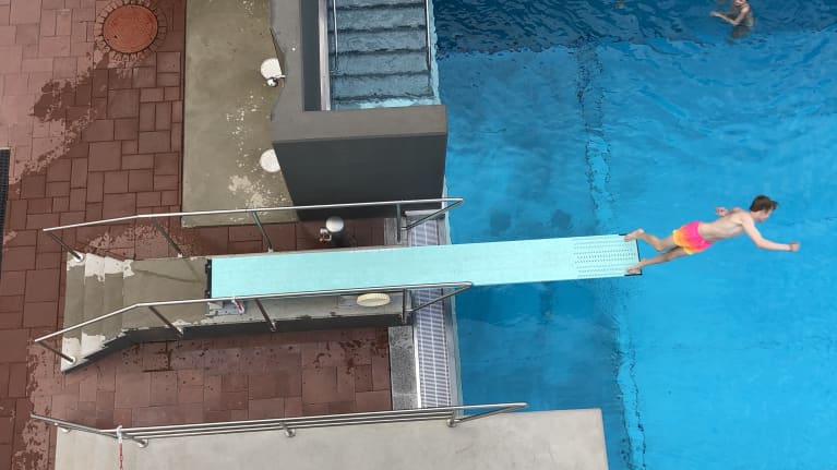 Poika hyppää ponnahduslaudalta uima-altaaseen.