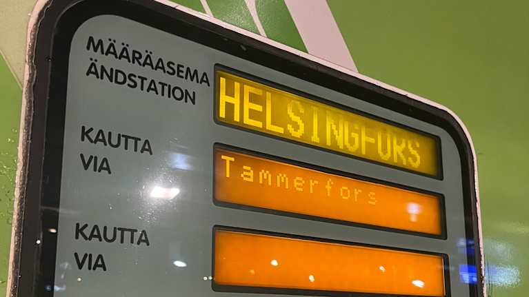 Kuvassa on VR:n kaukojunan näyttötaulu, josta pystyy katsomaan että juna on matkalla Helsinkiin, ja se pysähtyy välissä Tampereella.