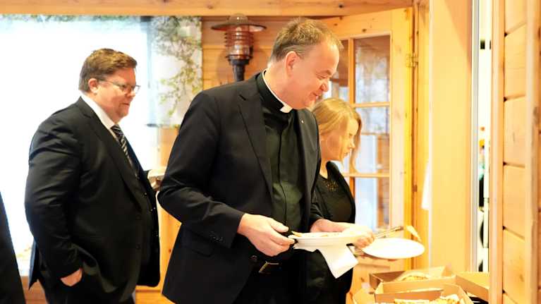 Kirkkoherra Kari Tiirola lautanen kädessä ottamassa pitsaa muistotilaisuudessa.
