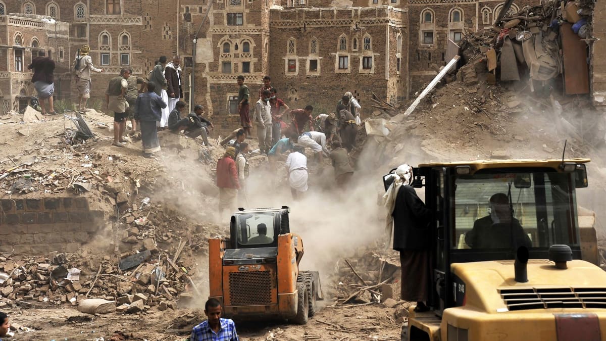Ihmiset tutkivat raunioita pommituksen jäljiltä Jemenin vanhassakaupungissa. Etualalla on iso ja pieni maansiirtokone.