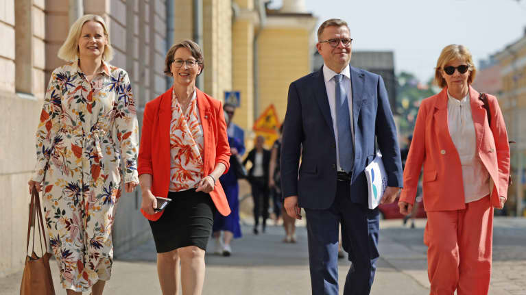 Riikka Purra, Sari Essayah, Petteri Orpo ja Anna-Maja Henriksson kävelee kadulla aurinkoisena päivänä.