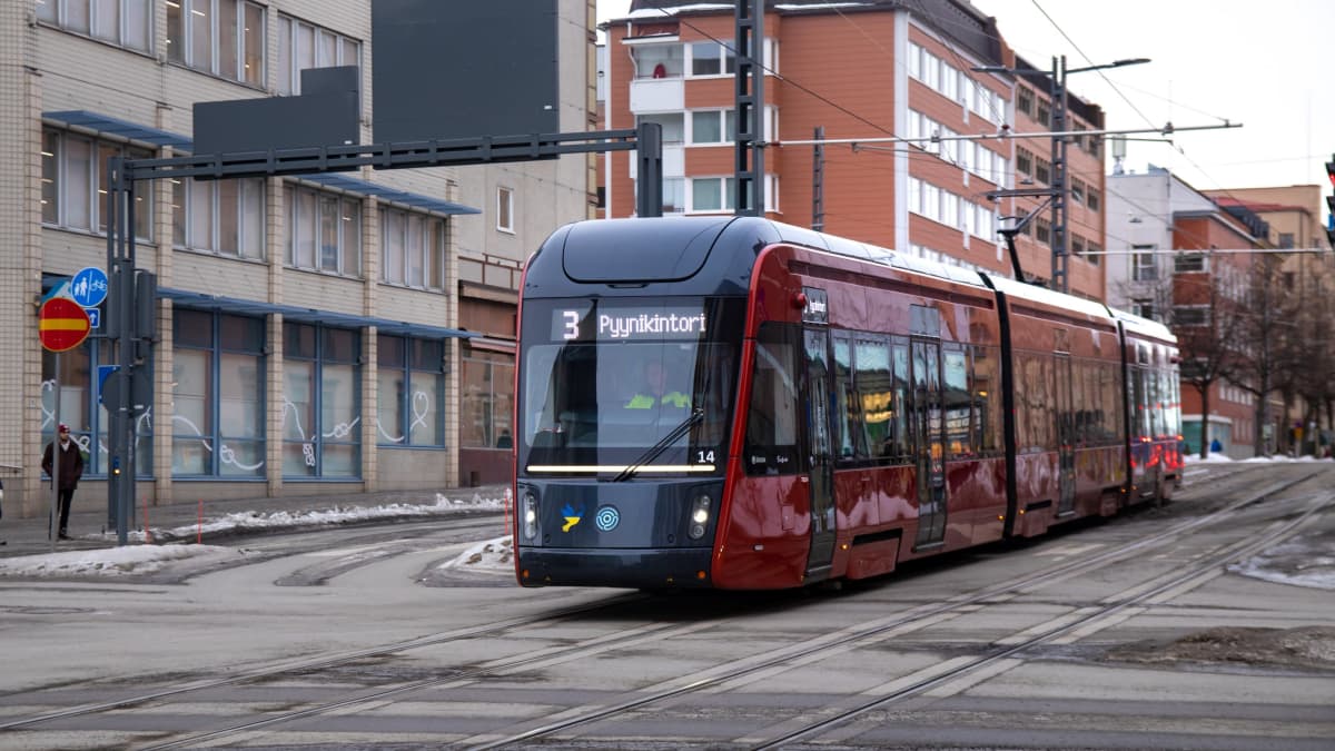 Punainen ratikka kulkemassa Itsenäisyydenkatua pitkin. Ambulanssi kulkemassa Tampereen Itsenäisyydenkatua pitkin. Ympäristö on lumen ja hiekan sekoittumisesta sotkuinen ja aavistuksen harmaa.
