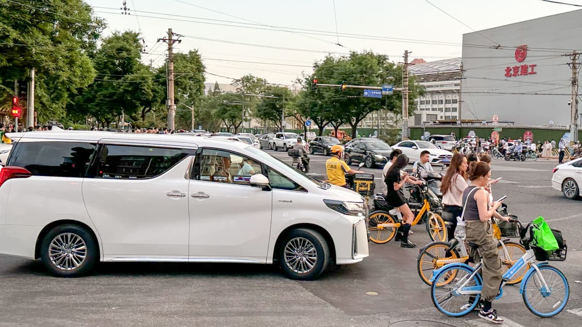 Valkoinen auto ja pyöräilijöitä odottamassa risteyksessä Pekingissä.