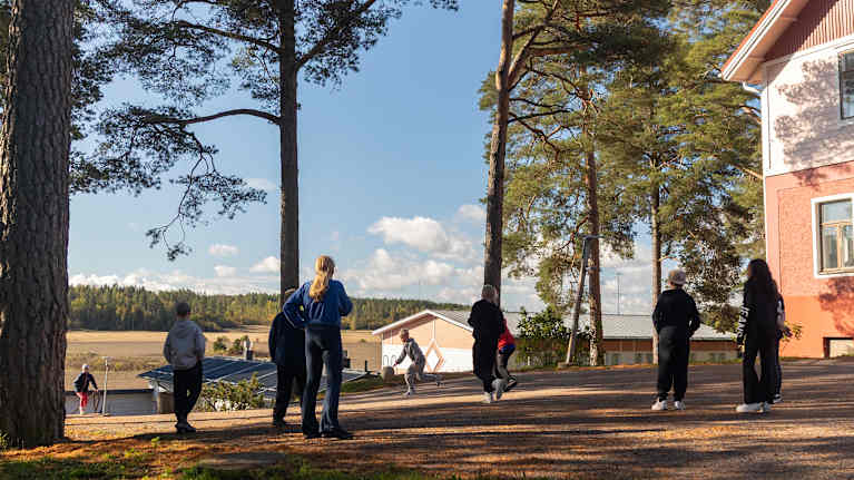 Oppilaita pelaamassa koulun pihalla, taustalla näkyy peltomaisema.