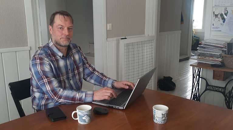 Man och dator vid köksbord.