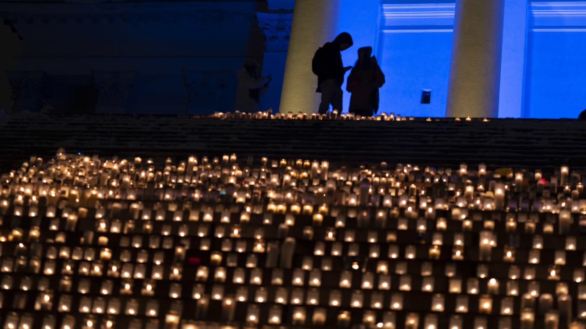 Tuomiokirkon portaille on laskettu paljon kynttilöitä. Rakennusta valaisee sininen valo. Portaiden yläpäässä kahden ihmisen siluetti.