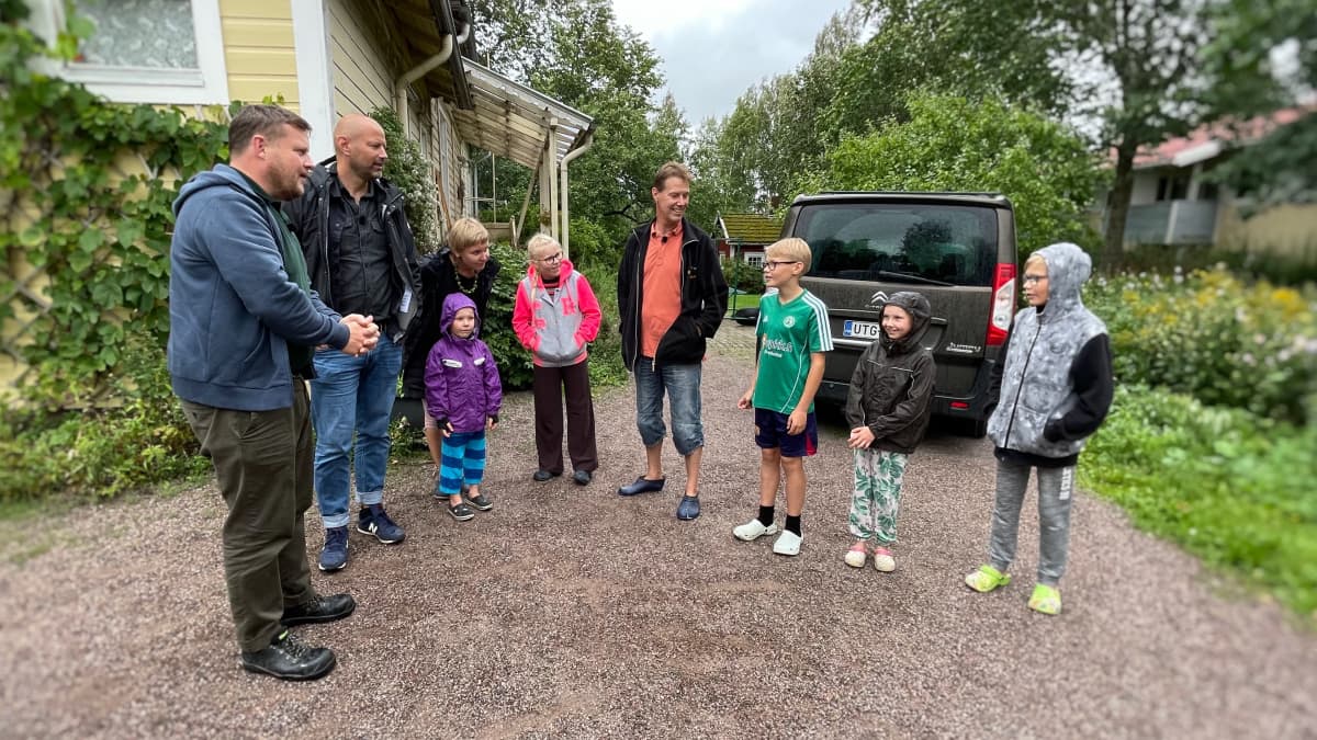 Nio personer står ute på en gård och diskuterar.