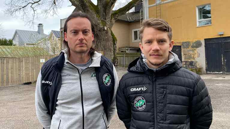 Två män står bredvid varandra med en stor ek i bakgrunden.