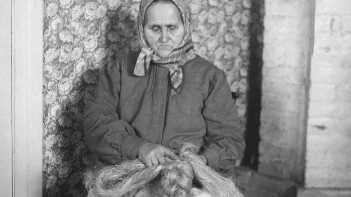 Vanha kuva, jossa nainen letittää pellavaa.