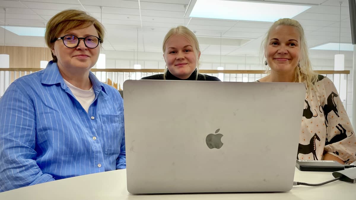 Olga Filippova, Heini Wilde ja Maria Pikkarainen istuvat pyöreän pöydän ääressä edessään auki oleva kannettava tietokone.