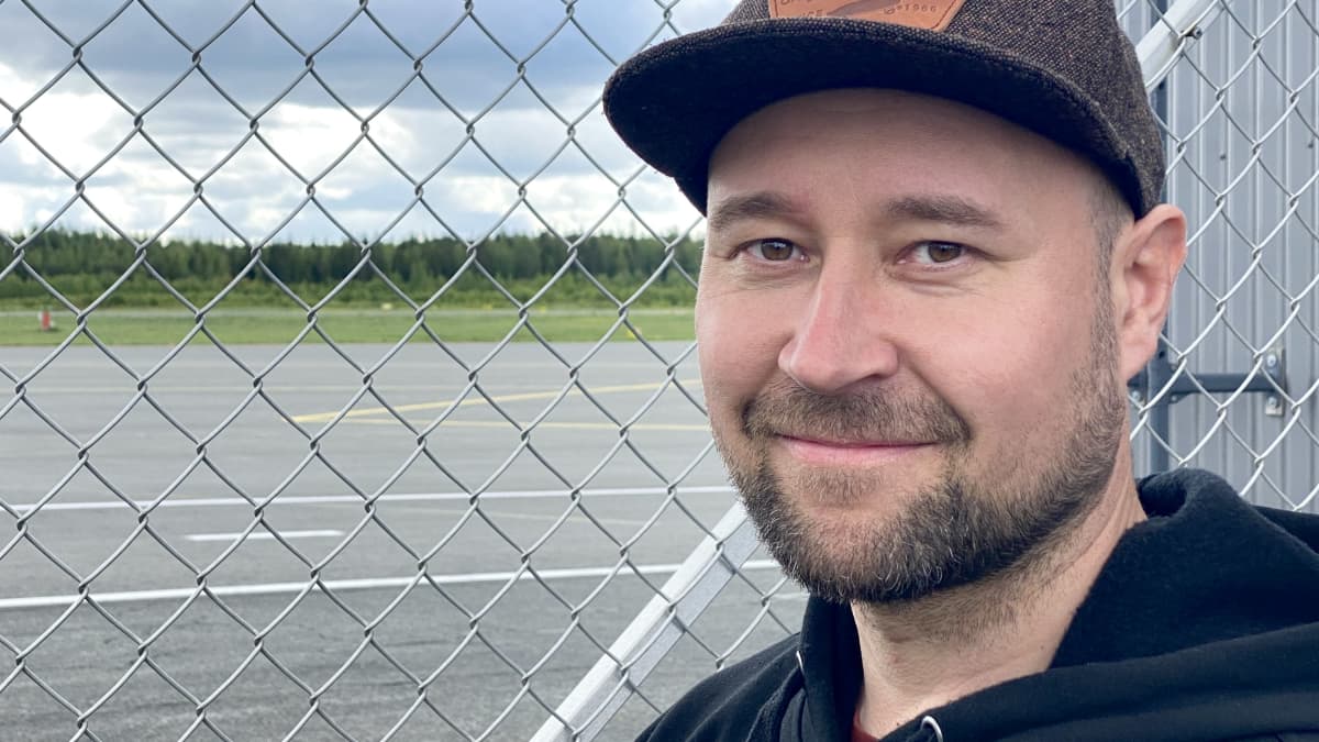Lentokentän verkkoaidan vieressä seisova Tommi Tapio katsoo kameraan hymyillen.