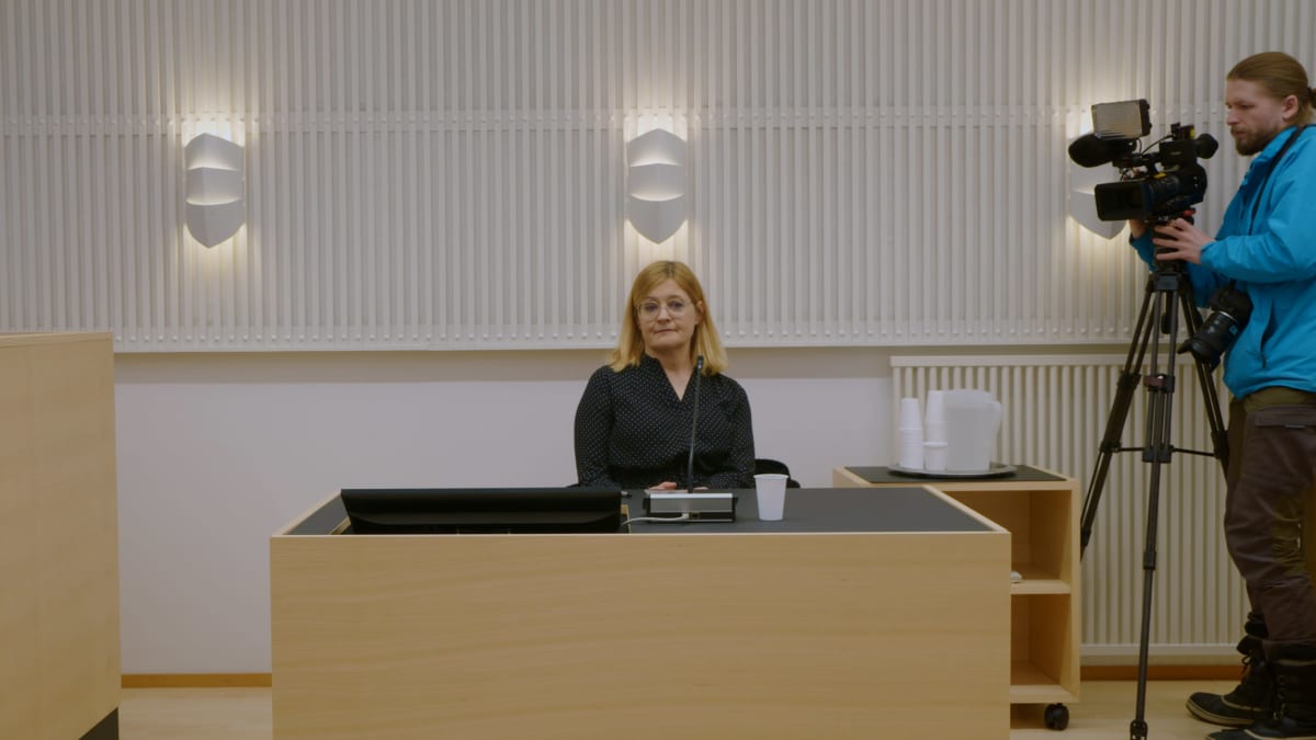 Anna Mäkelä istuu oikeudessa ison pöydän ääressä, Ylen kuvaaja kuvaa häntä videokameralla.