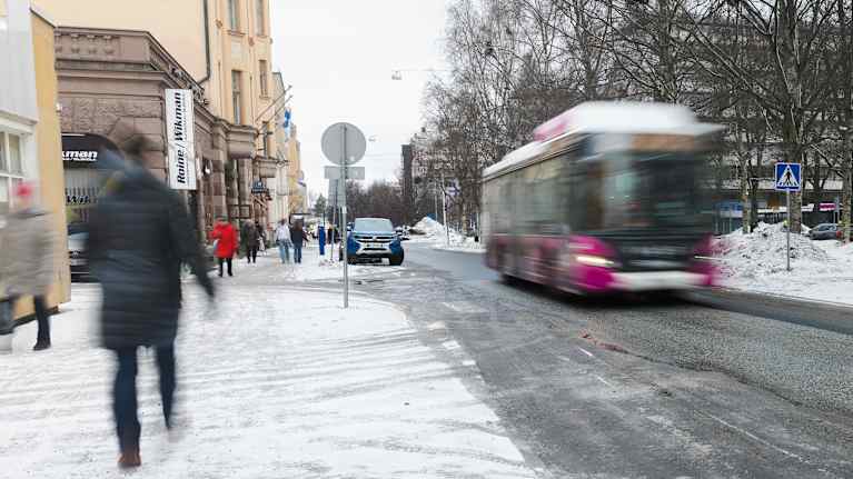 Buss kör längs gata med folk promenerande längs trottoar