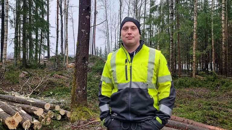 En man står bland stockar i skogen.