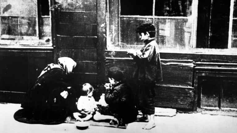 Nainen ja lapset seinänvieressä kadulla.