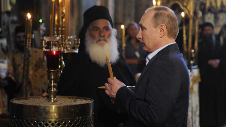 Putin sytyttää kynttilän kirkossa Kreikassa. 
