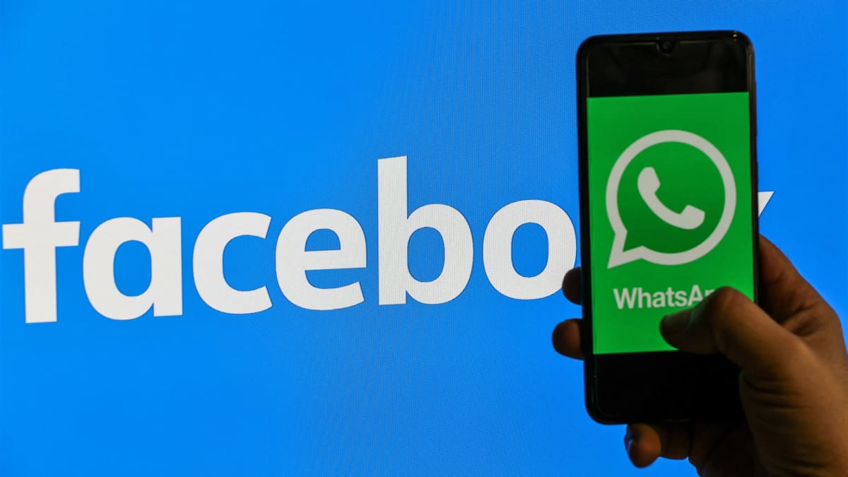 Kuvassa käsi pitelee kännykkää, jonka ruudulla nälyy Whatsapp-palvelun vihreä logo. Taustalla on Facebookin valkoinen teksti sinisellä pohjalla.