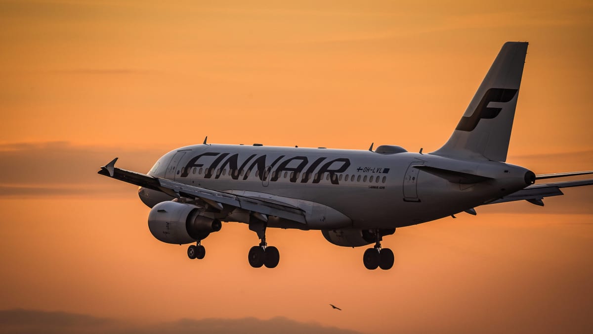 Ett Finnairplan flyger under en solnedgång. Himlen är orange.