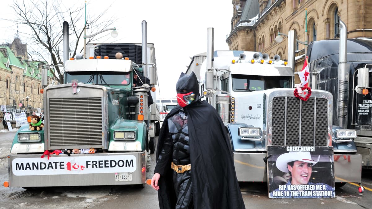 Batman-asuinen mielenosoittaja seisoo kahden ison rekan edessä.