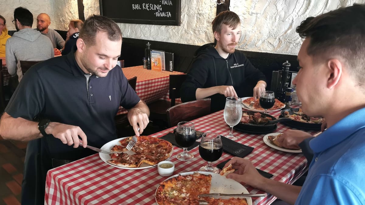 Mies syö pizzaa työkavereidensa kanssa Pizzeria Napolissa.