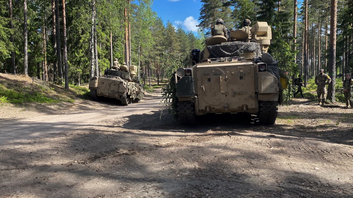 Kaksi panssarivaunua tiellä ja vieressä maastopukuisia sotilaita.